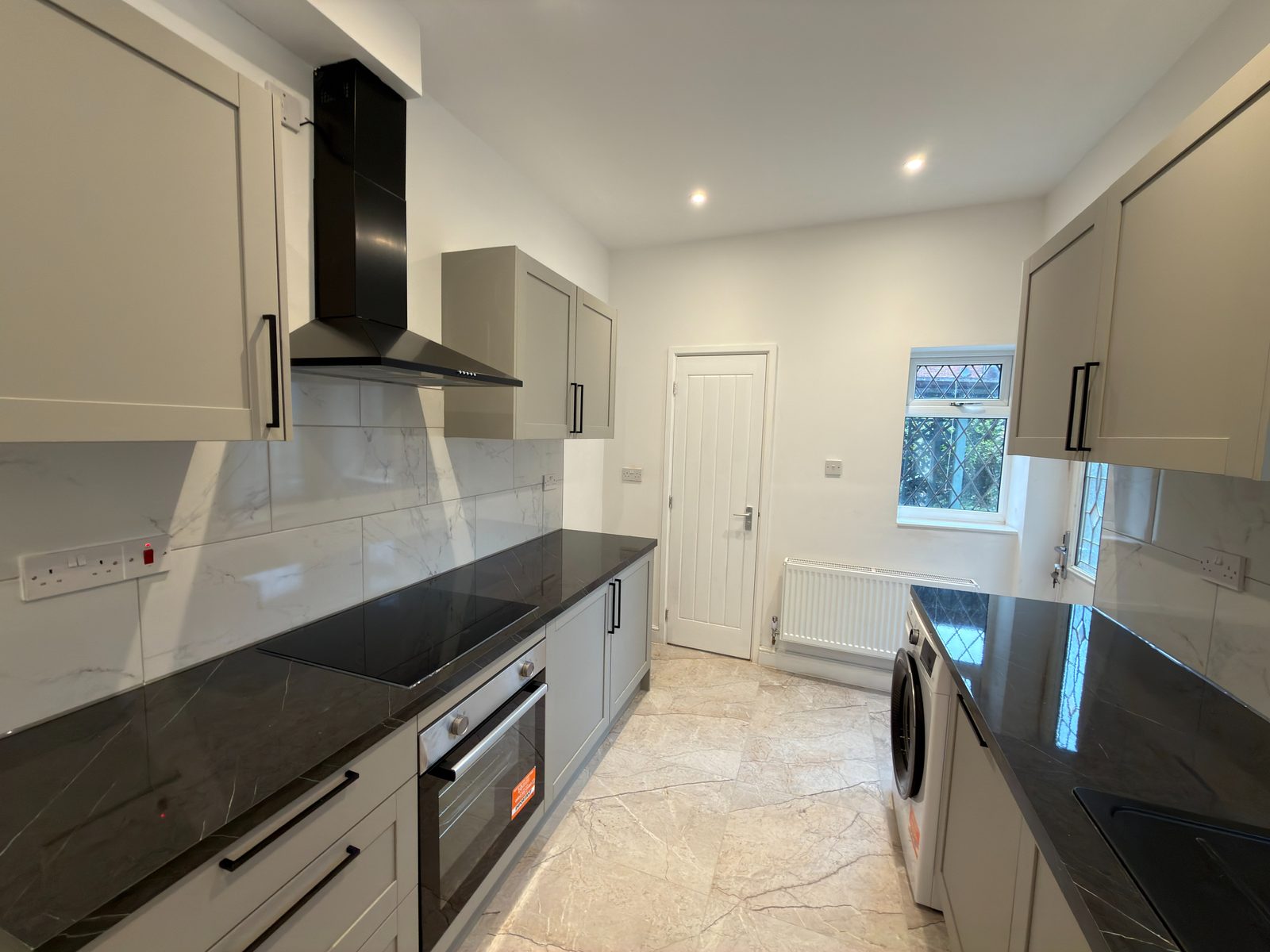 Refurbished kitchen with grey shaker units, black worktops and marble splashback